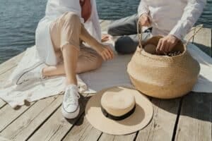 femme en baskets blanches assise sur un quai en bois a cote de chapeau marron