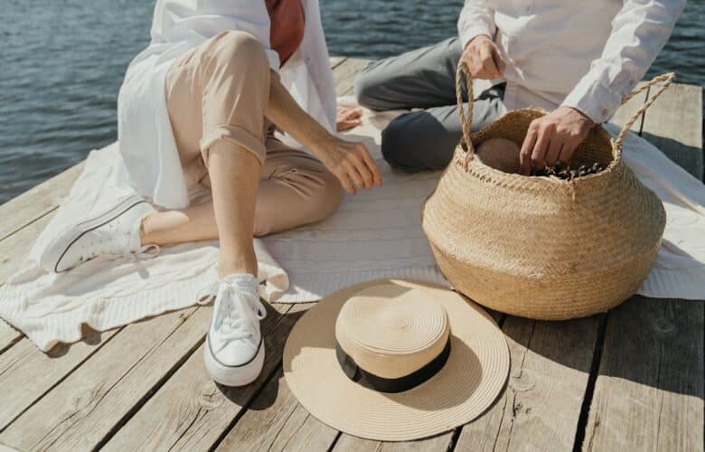 femme en baskets blanches assise sur un quai en bois a cote de chapeau marron